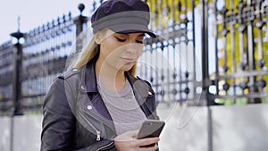 A young and attractive woman walks down the street and prints a message on the smartphone, the lady is holding a phone