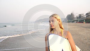 Young attractive woman walks in the morning along the sandy beach with a surfboard