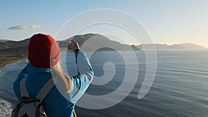 Young Attractive Woman Watching Sunset or Sunrise Over Bay from Top of the Mountain, Girl Takes Panorama Photos On Phone