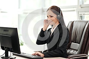 A young attractive woman wearing a black jacket in a black jacket is sitting at her desk in a executive chair. Holds a