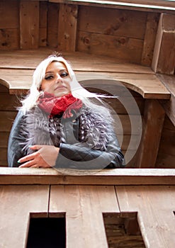 A young attractive woman wearing fur black jacket standing on background of wooden house.