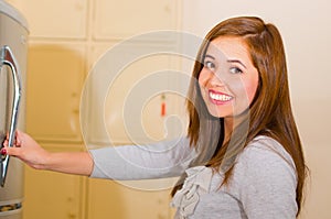Young attractive woman wearing grey sweater smiling and opening metal locker door, rack of lockers stacked