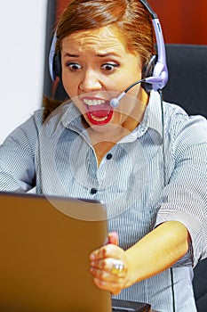 Young attractive woman wearing office clothes and headset sitting by desk looking at computer screen, grabbing laptop
