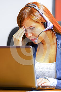 Young attractive woman wearing office clothes and headset sitting by desk looking at computer screen, working with