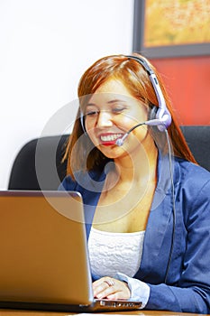 Young attractive woman wearing office clothes and headset sitting by desk looking at computer screen, working with