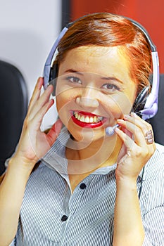 Young attractive woman wearing office clothes and headset sitting by desk looking at computer screen, working with