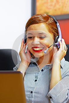 Young attractive woman wearing office clothes and headset sitting by desk looking at computer screen, working with