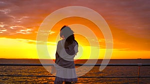 Young attractive woman wearing white dress and hat posing on sea background at amazing sunset