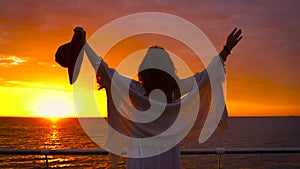Young attractive woman wearing white dress and hat posing on sea background at amazing sunset