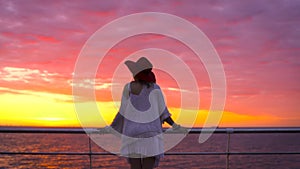 Young attractive woman wearing white dress and hat posing on sea background at amazing sunset