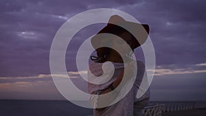 Young attractive woman wearing white dress and hat posing on sea background at amazing sunset