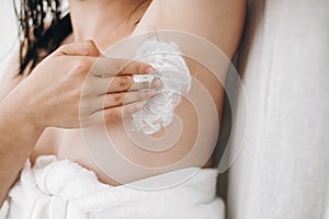 Young attractive woman in white towel applying shaving cream on armpit for depilation in home bathroom. Skin care. Hair Removal