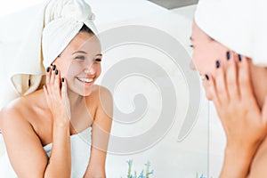 Young attractive woman with white towel on head and body with reflection in mirror in bathroom. Female smile and look at