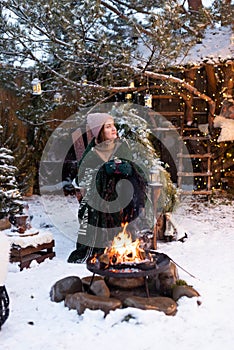 Young attractive woman in winter clothes sitting in a armchair, warming herself by the fire