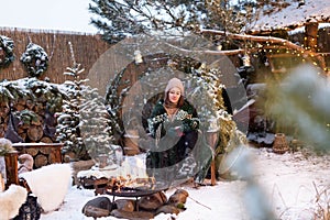 Young attractive woman in winter clothes sitting in a armchair, warming herself by the fire