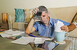 Young attractive worried and stressed man at home calculating month tax expenses with calculator accounting payments doing bank pa