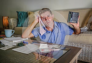 Young attractive worried and stressed man at home calculating month tax expenses with calculator accounting payments doing bank pa