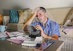 Young attractive worried and stressed man at home calculating month tax expenses with calculator accounting payments doing bank pa