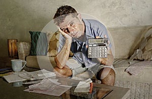 Young attractive worried and stressed man at home calculating month tax expenses with calculator accounting payments doing bank pa