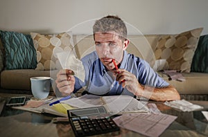 Young attractive worried and stressed man at home calculating month tax expenses with calculator accounting payments doing bank pa