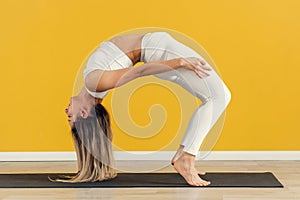 Young attractive yogi woman practicing bridge pose without arms, stretching in Urdhva Dhanurasana exercise on yellow