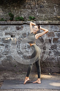 Young attractive yogi woman in sport wear practicing yoga, working out, cool urban style, grey studio background