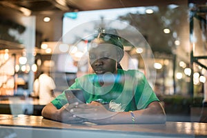 Young authentic black woman sitting with phone in city coffee shop at night