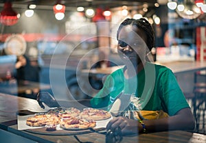 Young authentic black woman sitting with phone in city coffee shop at night