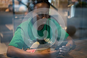 Young authentic black woman sitting with phone in city coffee shop at night