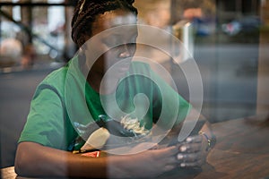 Young authentic black woman sitting with phone in city coffee shop at night