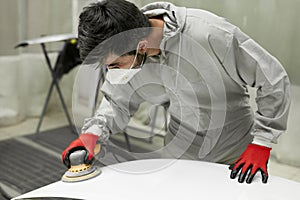 Young auto mechanic man buffing and polishing car holding polisher in hand