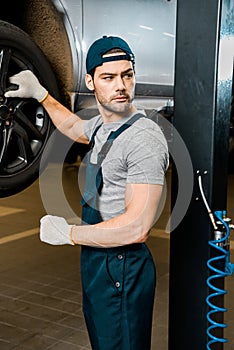 young auto mechanic in protective gloves standing at automobile