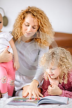 Young awesome mommy showing book to her children