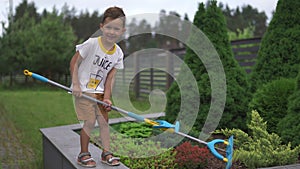 Young baby boy son slashing bushes with a mop swab in a garden with toys - Family values warm color summer scene