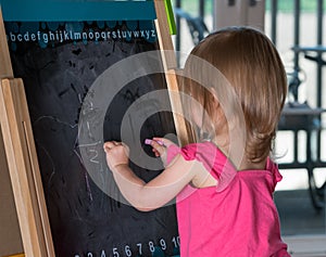 Young baby girl drawing at blackboard