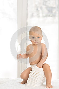 Young baby sitting on pile of disposable diapers