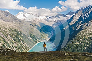 Young backpacker boy with the back at the camera watching a beautiful view over a lake in the Alps, scenic mountains in the