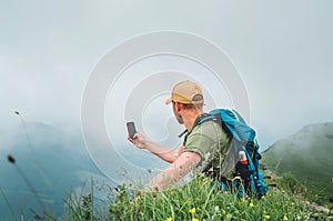 Young backpacker man taking picture of  cloudy valley bottom using smartphone during walking by the foggy cloudy weather mountain