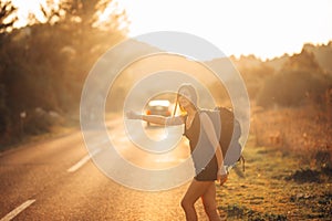 Young backpacking adventurous woman hitchhiking on the road. Stopping a car with a thumb. Travel lifestyle. Low budget traveling photo