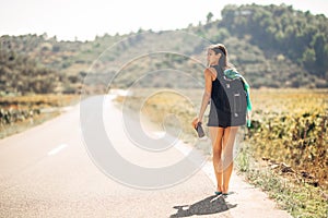Young backpacking adventurous woman hitchhiking on the road.Traveling backpacks volume,packing essentials.Travel lifestyle photo