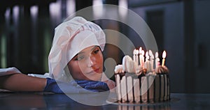 A young baker lady wearing a cookers hat , stares intensely at the cake with wonder