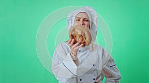 Young baker woman playing in front of the camera with a fresh french pretzel inside of a green studio she have a large