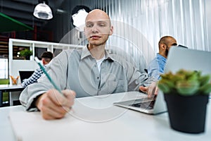Young bald business man sitting at desk in office, working on computer