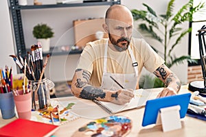 Young bald man artist drawing on notebook looking touchpad at art studio