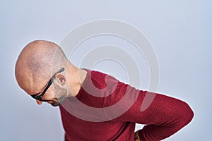 Young bald man with beard standing over white background wearing glasses suffering of backache, touching back with hand, muscular