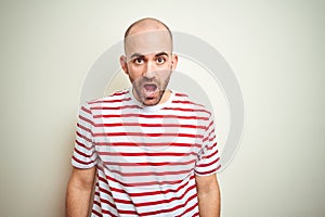 Young bald man with beard wearing casual striped red t-shirt over white isolated background afraid and shocked with surprise and