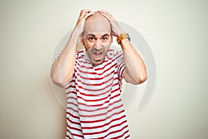 Young bald man with beard wearing casual striped red t-shirt over white isolated background Crazy and scared with hands on head,