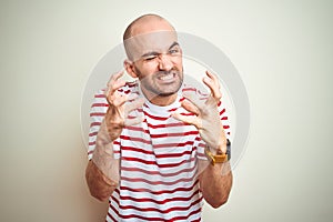 Young bald man with beard wearing casual striped red t-shirt over white isolated background Shouting frustrated with rage, hands