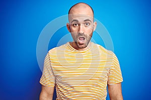Young bald man with beard wearing casual t-shirt over blue isolated background afraid and shocked with surprise expression, fear