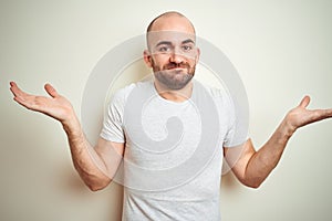 Young bald man with beard wearing casual white t-shirt over isolated background clueless and confused expression with arms and